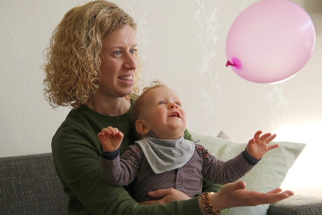 Mother relaxing at home while playing with her baby, representing a peaceful and comfortable Mother’s Day celebration